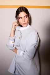 Camisa celeste a rayas verticales azules y marrones, con cuello blanco, cierre frontal con botones dorados y volantes verticales.