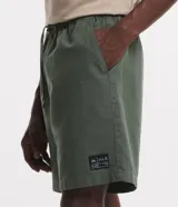 Bermuda masculina color marrón, confeccionada en tejido plano de algodón texturizado con poliéster. Presenta cintura elástica con cordón de ajuste y un tag de marca en el lateral inferior.