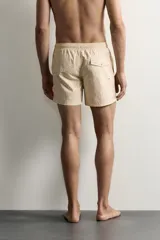 Short de baño de tejido técnico en color beige con estampado paisley en tonos claros y naranjas. Cuenta con cintura elástica con cordón ajustable, bolsillos laterales y forro interior.