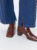 Botas de caña media color marrón, confeccionadas en cuero con acabado brillante. Presentan punta cuadrada, taco de madera y un distintivo bordado decorativo en color rojo que recorre el empeine hasta la punta.