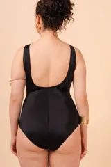 Malla entera de traje de baño, color negro, con escote en V profundo ribeteado en blanco. Presenta un cinturón blanco que se une en el centro con una argolla metálica dorada. Tiene tirantes anchos y un bolsillo interno para copa removible.