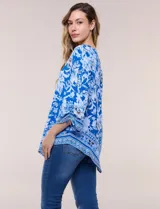 Blusa de gasa azul con estampado floral y geométrico estilo pañuelo, escote redondo, mangas tres cuartos amplias con jareta ajustable y ruedo asimétrico en punta.