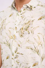 Camisa blanca con estampado de hojas verdes y marrones, de manga corta y cuello clásico.