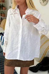 Camisa blanca de lino con botones, cuello clásico, mangas largas con puños abotonados y apliques de encaje en forma de estrella en el pecho y en los puños.