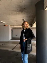 Camisa larga negra con cuello clásico, cierre frontal con botones a presión, mangas largas con puños de cuero y bolsillos de cuero con pespuntes blancos.