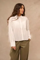 Camisa blanca de manga larga con diseño bordado y calado en patrón de rayas verticales. Posee cuello clásico, cierre frontal con botones y puños anchos.