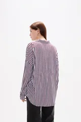 Camisa de corte holgado con estampado de rayas verticales en tonos bordó y blanco. Presenta cuello clásico, cierre frontal con botones, mangas largas con puños abotonados y un bolsillo frontal en el pecho.