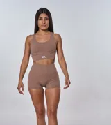 Conjunto deportivo compuesto por un top de escote redondo con espalda estilo nadador y un short de tiro alto. Ambas piezas son de color beige oscuro y cuentan con el logo de la marca estampado en blanco.