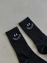 Par de medias largas negras con diseño de carita feliz y texto "BERKAMO" en blanco en la parte superior.