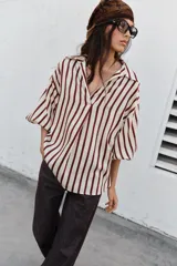 Camisa de cuello solapa con escote en pico, manga abullonada por debajo del codo con puños elásticos y diseño a rayas verticales.