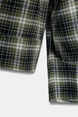 Camisa de corte oversize confeccionada en algodón, con estampado de cuadros en tonos verde, negro y blanco. Presenta cuello solapa, cierre frontal con botones, manga larga con puños y bajo asimétrico.