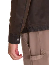 Chaqueta de estilo chore en tejido de sarga encerada color marrón, con cierre frontal metálico, cuello camisero y bolsillo con cierre en el pecho. Presenta un diseño de corte clásico con forro interno estampado.