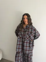Conjunto de camisa y pantalón de viyela a cuadros en tonos marrón, blanco y azul. La camisa es oversize de manga larga con bolsillos frontales y cierre de botones. El pantalón es recto y holgado.