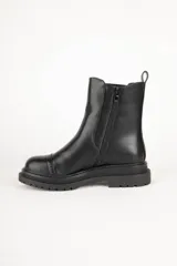 Bota Chelsea de cuero sintético color negro, con elástico lateral, puntera redondeada con detalle de perforaciones y suela track.