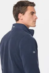 Buzo de micro polar con interior térmico, cuello alto y cierre frontal parcial. Presenta paneles de taslón al tono en el frente y cuello, con bolsillos laterales con cierre y detalle de logo en la manga.