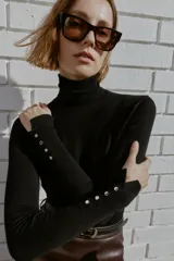 Jersey de punto liso en color beige, con cuello alto y manga larga con detalle de botones metálicos en los puños.