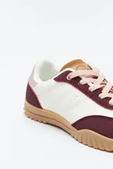 Zapatilla urbana de mujer con silueta retro, combinando paneles de cuero blanco y gamuza gris claro. Posee un talón trasero en gamuza negra y suela robusta de goma color caramelo con relieve.