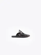 Mocasín tipo slide color marrón oscuro con efecto gastado, confeccionado en cuero vacuno. Presenta detalles de picado en la capellada y laterales, forrería de cuero vacuno, hebilla y puntera metálica.