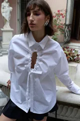 Camisa oversize de manga larga en color blanco, confeccionada en algodón. Presenta cuello clásico, puños abotonados y una abertura central ovalada con jaretas ajustables que permiten fruncir la prenda.