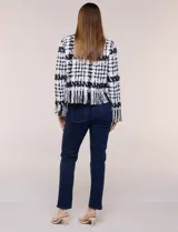 Chaqueta de tweed en blanco y negro con patrón de cuadros, escote redondo, bolsillos frontales con botones metálicos y flecos decorativos en los bordes y puños.