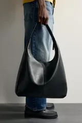 Bolso tipo shopper color negro con diseño liso, asa de hombro y compartimento principal con cierre de cremallera.