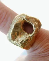 Anillo dorado con forma irregular y un agujero en el centro.