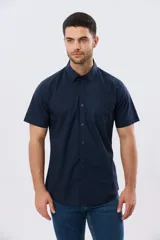 Camisa lisa de algodón azul marino, de manga corta, con cuello camisero, cierre frontal de botones y un bolsillo aplicado en el pecho.