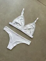 Conjunto de lencería compuesto por un bralette sin taza con detalles de encaje en los bordes y una bombacha tipo less, ambos en color blanco.