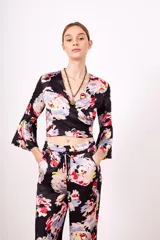 Camisa negra con estampado floral multicolor, escote en V cruzado y mangas acampanadas.