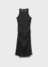Vestido midi de tejido fluido con estampado de lunares blancos sobre fondo negro. Presenta un diseño entallado sin mangas con escote redondo, tirantes anchos y un detalle de fruncido lateral con lazo que crea un efecto drapeado. Incluye cierre de cremallera invisible en la parte posterior.