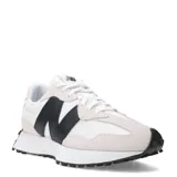 Championes urbanos New Balance modelo 327, con diseño inspirado en el running de los años 70. Presentan una combinación de paneles de gamuza en tono beige claro y malla blanca, con el logo 'N' sobredimensionado en color negro en el lateral. Incluyen una entresuela de espuma blanca y una suela exterior de goma negra con patrón tipo trail que se extiende hacia el talón.