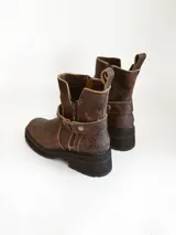 Bota corta de cuero vacuno en color chocolate con efecto desgastado. Presenta una suela track de goma negra, detalle de pulsera desmontable con tachas metálicas y cierre lateral.