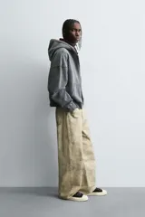 Pantalón de corte baggy fit confeccionado en tejido de algodón con textura y efecto lavado. Presenta diseño de cinco bolsillos, cierre frontal con cremallera y botón.