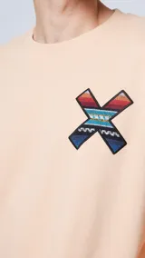 Sudadera color durazno de corte holgado con cuello redondo, puños y bajo acanalados. Estampado en la espalda con una cruz formada por motivos étnicos y logo de la marca en la parte superior.