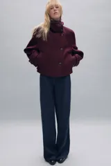 Abrigo corto de paño con mezcla de lana, color bordó. Presenta cuello subido, cierre frontal cruzado con botones, mangas largas con trabillas decorativas y bolsillos laterales de vivo.