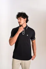 Polo de manga corta confeccionado en tejido interlock suave, color negro con detalles de vivos en color blanco en el cuello y las mangas. Presenta tapeta con botones y un bolsillo frontal con el logo bordado.