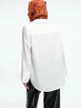 Camisa de corte oversize color bordó, con cuello clásico, cierre frontal de botones y mangas largas amplias con puños anchos. Presenta un diseño de caída fluida con bajo redondeado y levemente más largo en la parte posterior.