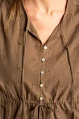 Blusa blanca de algodón con delicado bordado floral, mangas abullonadas de largo 3/4 y cierre frontal con botones y cordón ajustable en la cintura.