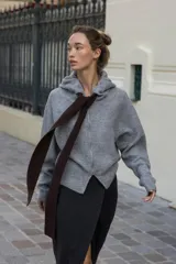 Chaqueta de punto con capucha, manga larga y cierre frontal con cremallera. Presenta un diseño en color beige con un lazo decorativo a contraste en color marrón oscuro en la zona del cuello.