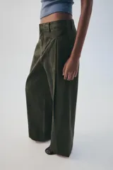 Pantalón verde militar de tiro medio, con bolsillos delanteros, pliegues y tejido con efecto lavado. Cuenta con cierre frontal con cremallera y gancho metálico.