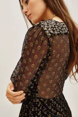 Vestido corto de manga larga con diseño semitransparente y estampado floral geométrico en tonos oscuros y dorados. Presenta un corte entallado en la cintura y una falda con caída fluida.