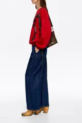 Bolso bandolera de gabardina con estampado de cuadros en tonos marrones y verdes, con asa de cinta negra regulable y logo de la marca estampado en la parte inferior.