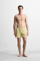 Short de baño confeccionado en tejido técnico, con diseño de rayas verticales amarillas y verdes sobre fondo blanco. Cuenta con cintura elástica ajustable con cordón, bolsillos laterales y bolsillo trasero con vivo.
