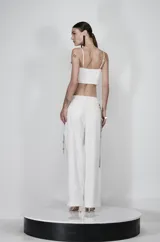 Pantalón blanco de corte amplio y fluido, con tiras colgantes de strass decorativas en los laterales.