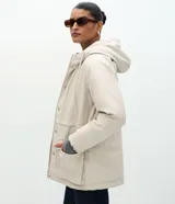 Campera parka de Marfinno confeccionada en PU con textura gomosa, color beige. Cuenta con capucha, forro interior de peluche sintético, cierre frontal con solapa y botones a presión, y bolsillos delanteros grandes con solapa.