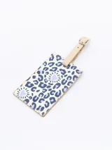 Identificador de maleta rectangular con estampado de animal print en tonos lila y blanco, con corazones. Tiene una correa ajustable de cuero sintético color beige con hebilla metálica.