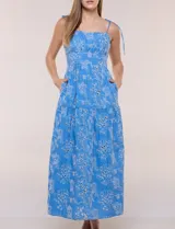 Vestido midi color azul con bordado broderie floral en tono blanco, escote recto con tirantes finos de lazo para anudar, corte ajustado en la cintura y falda escalonada holgada con bolsillos laterales.