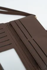 Billetera negra de textura granulada con cierre de solapa y botón a presión metálico. Incluye una correa de muñeca extraíble.
