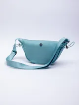 Riñonera semicircular color celeste de nylon con correa regulable, cierre superior y elásticos en los laterales.