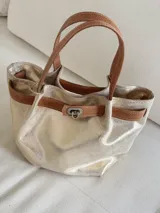 Cartera tipo mini bag de cuero con acabado metalizado dorado, asas de mano y detalle de tira marrón con cierre metálico frontal.